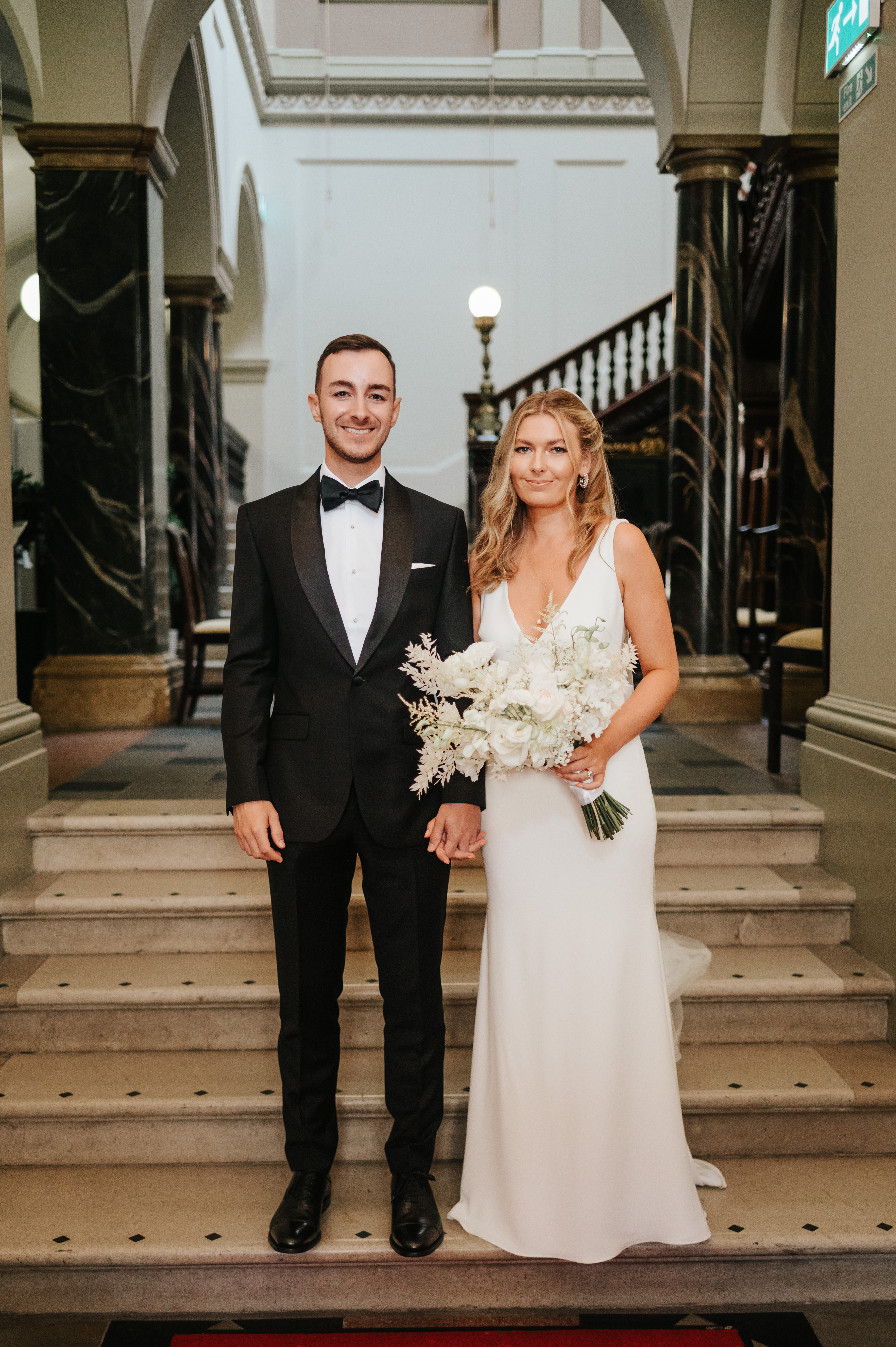 Wedding couple stand at the bottom of the Guildhall marble staircase